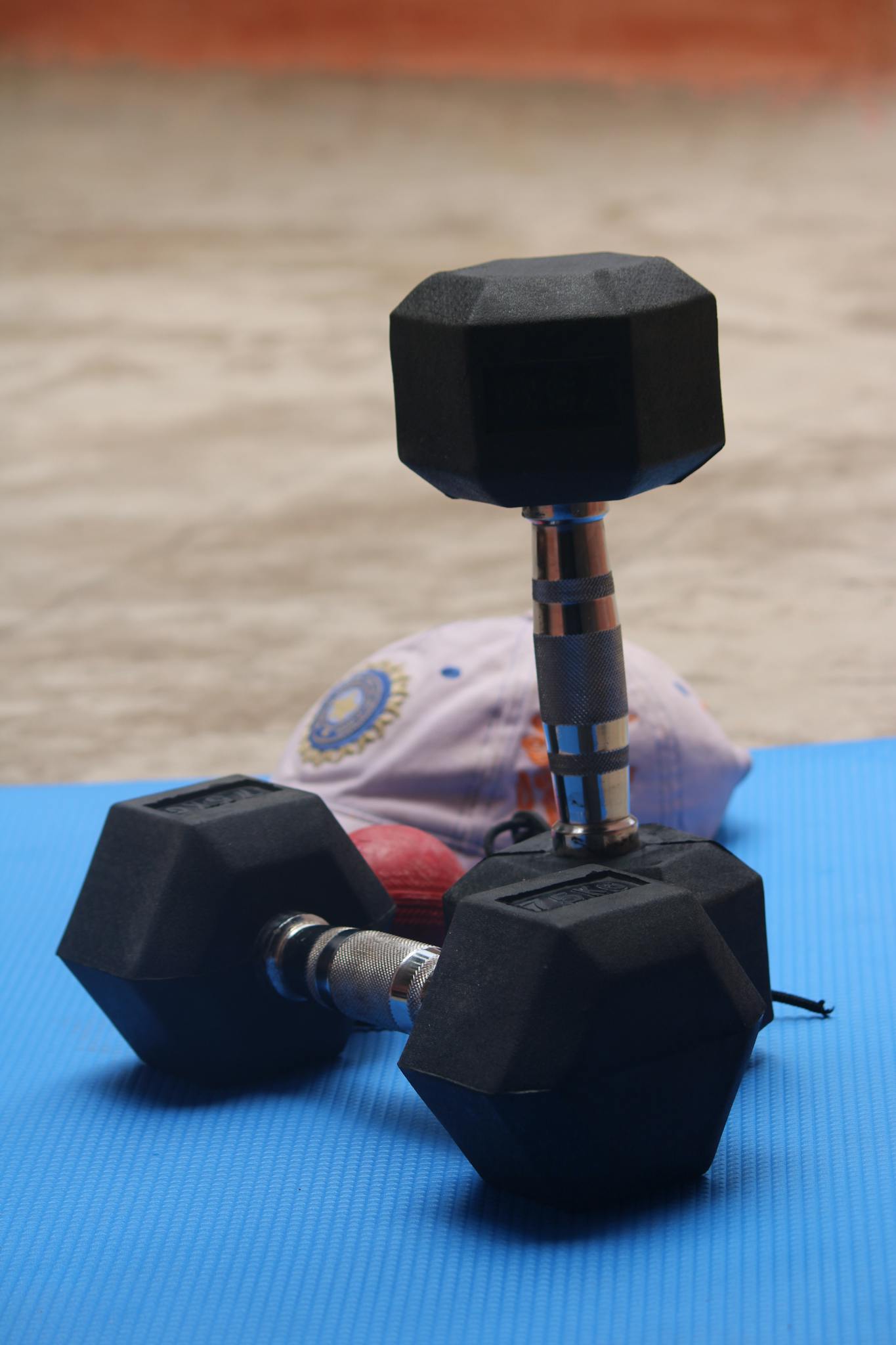 Close-up of black hexagonal dumbbells on a blue exercise mat indoors.